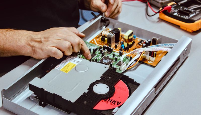 un lecteur DVD ouvert, une main y désigne un composant électronique